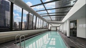 An indoor swimming pool with a city view, large windows, and a modern architectural design.