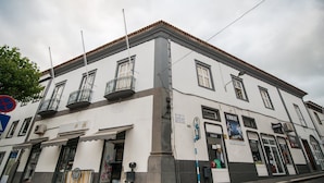 A white building with multiple windows and balconies, a storefront with a sign, and a cobblestone street. - GuestReady - O Ateneu - Room 8 (Ponta Delgada)