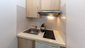 A compact kitchen with a sink, stove, and overhead ventilation hood. - Studio with Garden view 7G (Antibes)