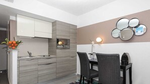 A modern kitchen with a built-in oven, a dining area with two chairs, and a wall-mounted mirror. - Studio with Garden view 7G (Antibes)