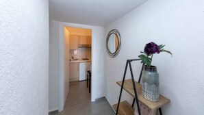 A hallway with a wooden shelf holding a vase with a flower, a mirror, and a staircase leading to a kitchen. - Studio with Garden view 7G (Antibes)