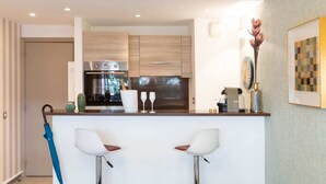 A modern kitchen with a built-in oven, two bar stools, and a small bar area. - Bright and Cosy 2 - Studio Apartment, Sleeps 2 (Antibes)