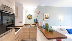 A modern kitchen with a built-in oven and stove, a sink, and wooden cabinets. There is a dining area with a table and chairs, and a bed with pillows and a blanket. - Bright and Cosy 2 - Studio Apartment, Sleeps 2 (Antibes)