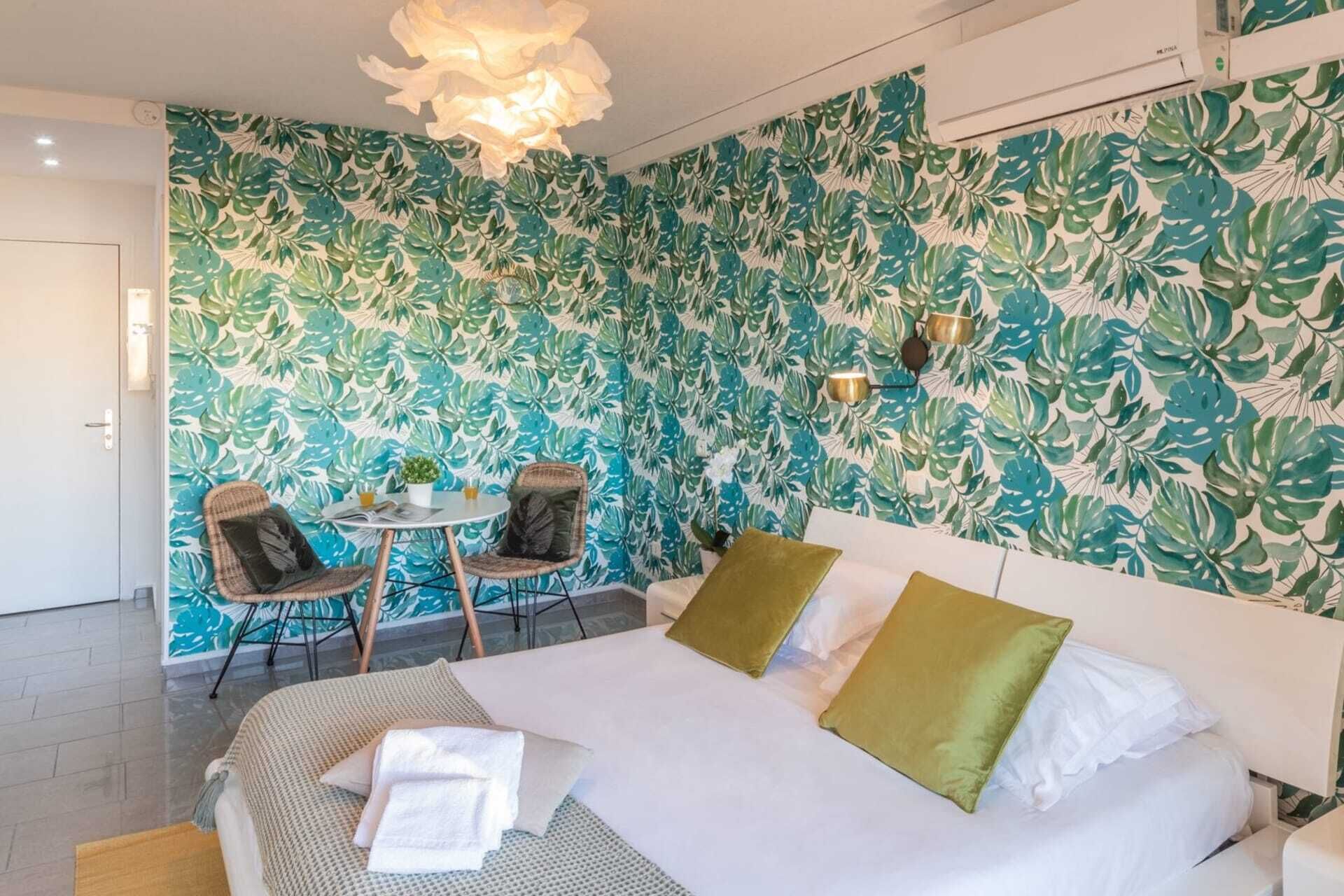 A hotel room with a bed, two chairs, a small table, and a wall with a leafy pattern.