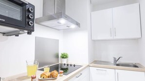 A modern kitchen with white cabinets, a black microwave, a stainless steel range hood, a sink, and a small potted plant. - Bright and Cosy 2 - Studio Apartment, Sleeps 2 (Antibes)