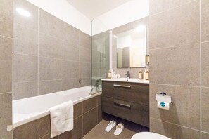 Une salle de bain moderne comprenant une baignoire, une douche à parois de verre, un meuble-lavabo avec un miroir et des toilettes.