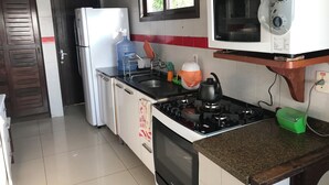Une cuisine compacte équipée d’un réfrigérateur, d’un four à micro-ondes, d’une cuisinière à gaz et d’un distributeur d’eau.