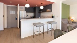 A modern kitchen with a white island, two bar stools, a refrigerator, and a clock on the wall. - Two-bedroom 1B - Two Bedroom Apartment, Sleeps 6 (Antibes)