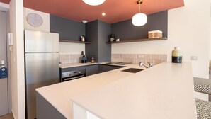 A modern kitchen with a refrigerator, oven, and sink. There are two pendant lights, a clock, and a shelf with kitchen items. - Two-bedroom 1B - Two Bedroom Apartment, Sleeps 6 (Antibes)