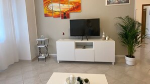 A modern living room with a white TV stand, a flat-screen TV, a white coffee table with decorative items, a potted plant, and artwork on the walls. - THE HOUSE OF CARLOTTA AND CAMILLA (Lazio)