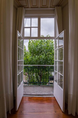 Un balcon ouvert donnant sur un arbre verdoyant et muni d’une rambarde en métal.