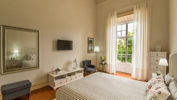 A bedroom with a large bed, a television, a chair, a dresser, and a window with curtains.