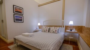Ein ordentlich eingerichtetes Schlafzimmer mit einem Bett, zwei Nachttischen, einem Beistelltisch und einem kleinen Tisch mit einer Lampe.