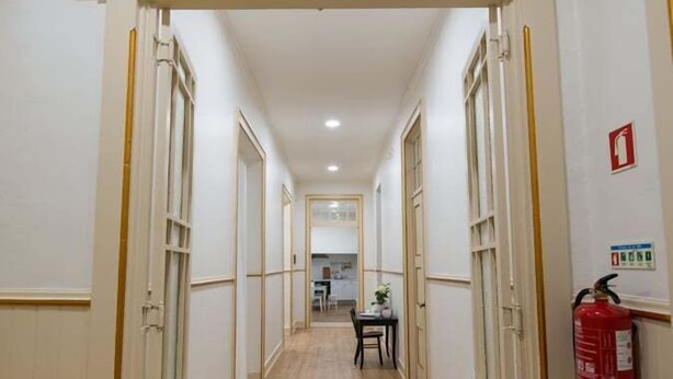 Un pasillo con piso de madera, paredes blancas y un arco decorativo. Hay un extintor en la pared derecha.