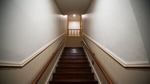 Eine Holztreppe mit weißen Wänden und einem Holgitter, die zu einer Zwischenebene mit einer Lampe führt.