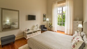 Ein Schlafzimmer mit einem großen Bett, einem Fernseher, einem Sessel, einer Kommode und einem Fenster mit Vorhängen.