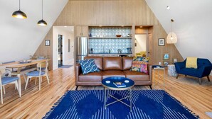 A loft-style living space with a dining area, a sofa with patterned cushions, a coffee table, and a kitchen area with patterned backsplash. - Modern and Secluded A-Frame with a Hot Tub for a Romantic Texas Hill Country Getaway (Wimberley)
