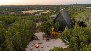 A modern building with a triangular roof surrounded by dense greenery. - Modern and Secluded A-Frame with a Hot Tub for a Romantic Texas Hill Country Getaway (Wimberley)