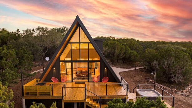 A modern A-frame cabin with large windows, a wooden deck, and a hot tub. - Modern and Secluded A-Frame with a Hot Tub for a Romantic Texas Hill Country Getaway (Wimberley)