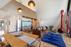 Una cocina moderna con armarios de madera, una zona de comedor con mesa y sillas, una sala de estar con sofá, y una chimenea roja.