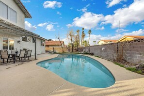 Ein Pool mit gewölbter Kante, eine Terrasse mit Tisch und Stühlen und eine Ziegelmauer.