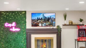 Ein Wohnzimmer mit Kamin, einer Neonreklame, einem Fernseher mit Stadtansicht und einer Spielmaschine.