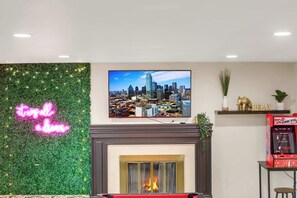 Ein Wohnzimmer mit Kamin, einer Neonreklame, einem Fernseher mit Stadtansicht und einer Spielmaschine.