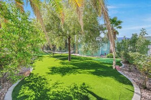 A well-maintained garden with a hammock, palm trees, and a clear sky.