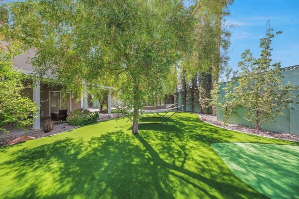 A well-maintained backyard with a lawn, a hammock, and a pergola.
