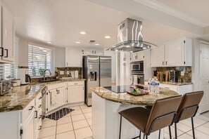 Une cuisine moderne avec des meubles blancs, des appareils en acier inoxydable, un Ăźlot central dotĂ© dâun comptoir en granit et un tapis Ă motifs noir et blanc.
