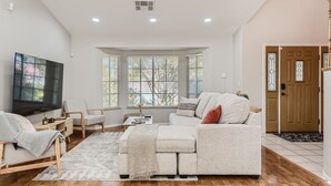 A spacious living room with a large flat-screen TV, a sofa, a coffee table, and a wooden floor. - Heated Pool with Cabana & GameRoom 15 Min to Strip (Las Vegas)