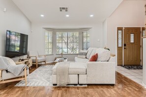 Un salon spacieux dotĂ© dâun grand tĂ©lĂ©viseur Ă Ă©cran plat, dâun canapĂ©, dâune table basse et dâun plancher en bois.