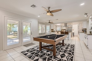 A pool table in a spacious room with a kitchen area, sliding glass doors, and ceiling fans. - Heated Pool with Cabana & GameRoom 15 Min to Strip (Las Vegas)