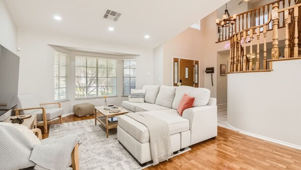 A spacious living room with a white sofa, wooden flooring, a ceiling fan, and a staircase. - Heated Pool with Cabana & GameRoom 15 Min to Strip (Las Vegas)