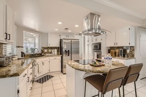 A modern kitchen with white cabinetry, stainless steel appliances, and a central island with bar stools.