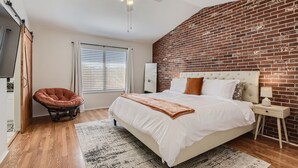 A bedroom with a brick wall, a bed, a chair, a ceiling fan, and a window with blinds. - Heated Pool with Cabana & GameRoom 15 Min to Strip (Las Vegas)