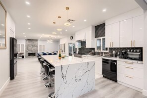 A modern kitchen with a marble island, black appliances, and a dining area with blue chairs.