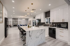 Una cocina moderna con una isla de mármol, armarios blancos y negros, y un comedor con sillas azules.