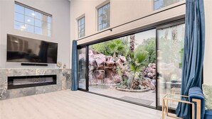 Ein modernes Wohnzimmer mit Fernseher, Kamin und einer großen Glasschiebetür zu einem Steingarten.