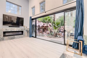 Una sala de estar moderna con un televisor de pantalla plana, chimenea y un gran ventanal que da a un jardín de rocas.