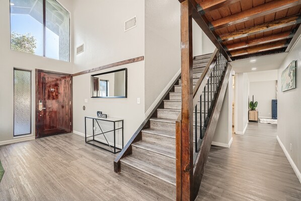 A spacious hallway with a wooden staircase, a large mirror, and a door with a textured glass panel.