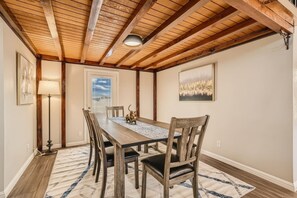 Un comedor con una mesa de madera, sillas, un tapete, una lámpara y obras de arte en las paredes.