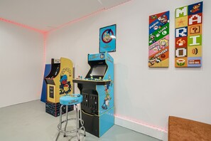 A room with arcade machines, a bar stool, and wall decorations featuring Mario and Luigi.