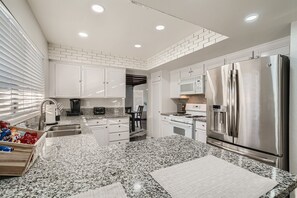 A modern kitchen with white cabinets, granite countertops, stainless steel appliances, and a brick accent wall.