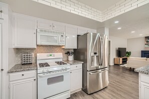 A kitchen with white cabinets, stainless steel appliances, and a brick backsplash.