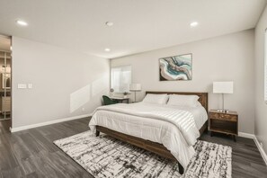 A bedroom with a bed, bedside tables, a desk, a chair, a window with blinds, and a painting on the wall.