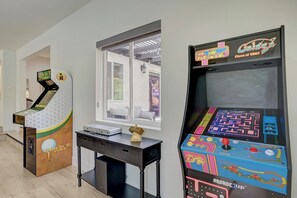 Two arcade machines, a window with a view, and a desk with a suitcase.