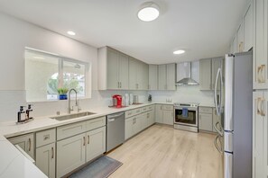 A modern kitchen with light-colored cabinets, a stainless steel oven, a refrigerator, and a window with a view of greenery outside.
