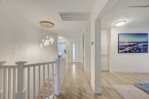 A hallway with a white railing, wooden flooring, recessed lighting, and a large landscape painting on the wall.