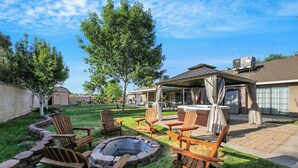 A backyard with a fire pit, wooden chairs, and a hot tub.